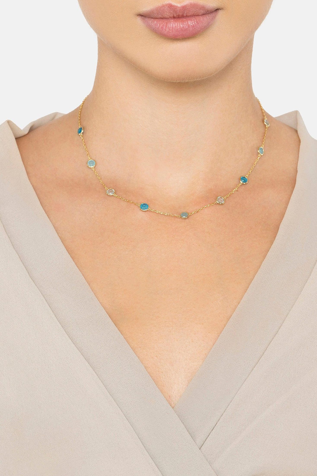 Gold-tone blue-stone necklace worn at the collarbone on a model