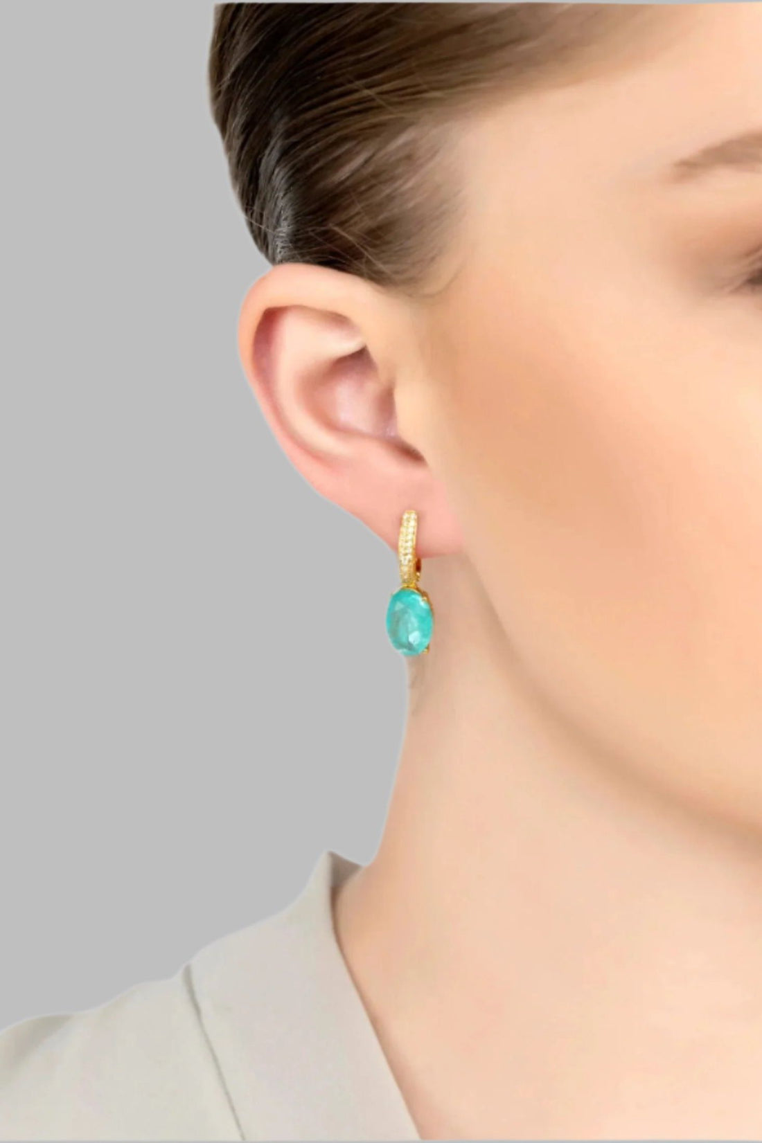 Oval drop earrings with gold setting and aqua stone, worn on the ear