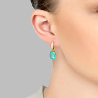 Oval drop earrings with gold setting and aqua stone, worn on the ear