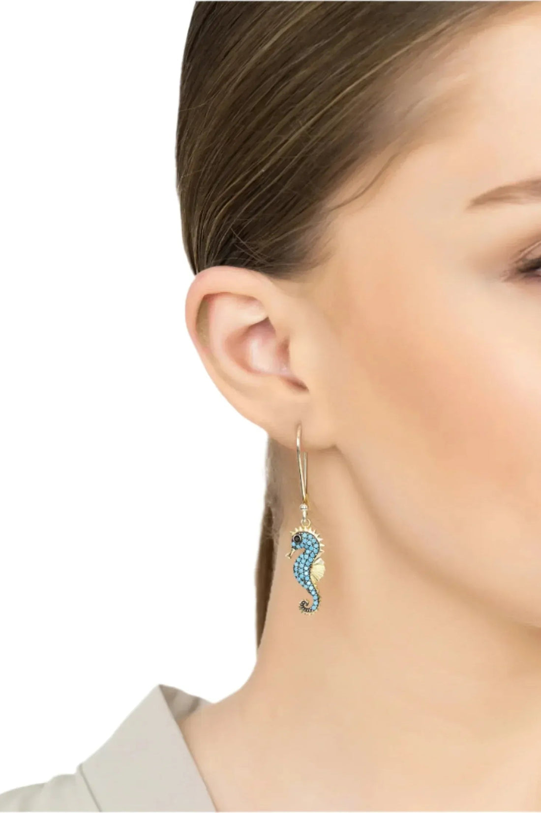 Turquoise seahorse drop earrings with gold-tone hook, close-up on side of face