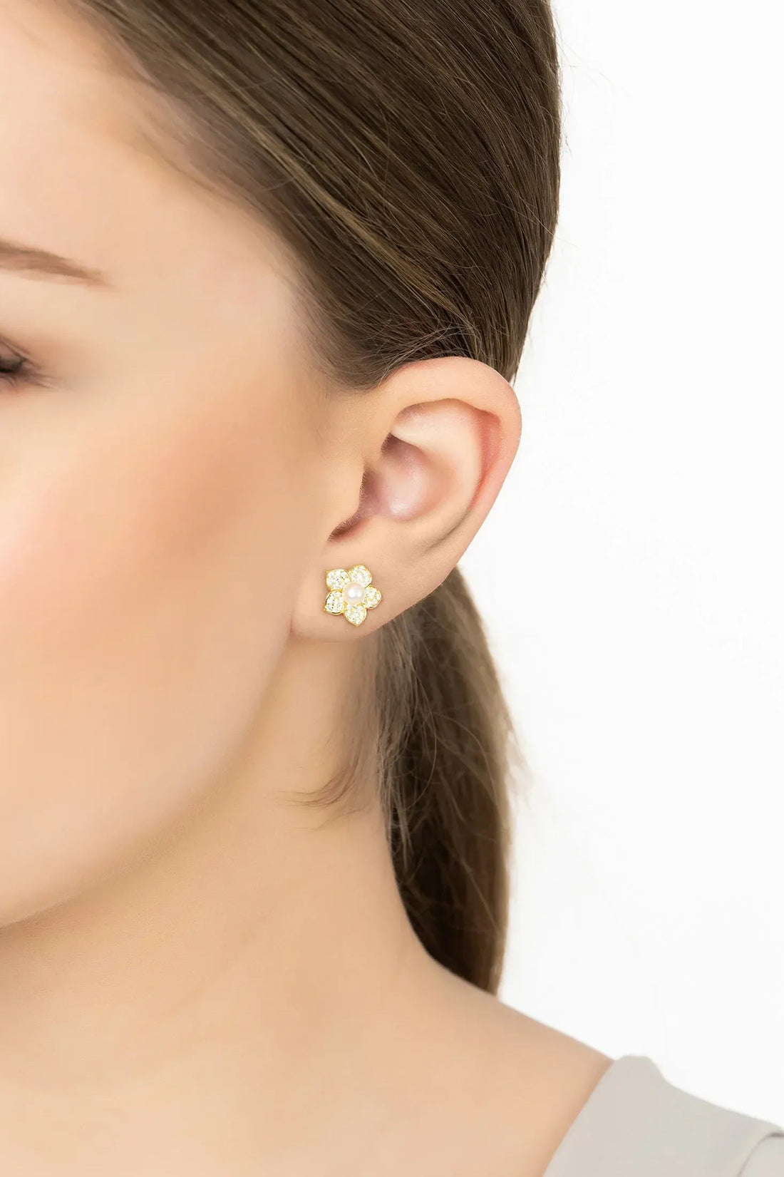 Gold pearl stud earrings with flower-shaped gemstone cluster on ear