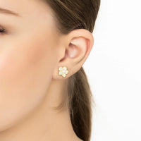 Gold pearl stud earrings with flower-shaped gemstone cluster on ear