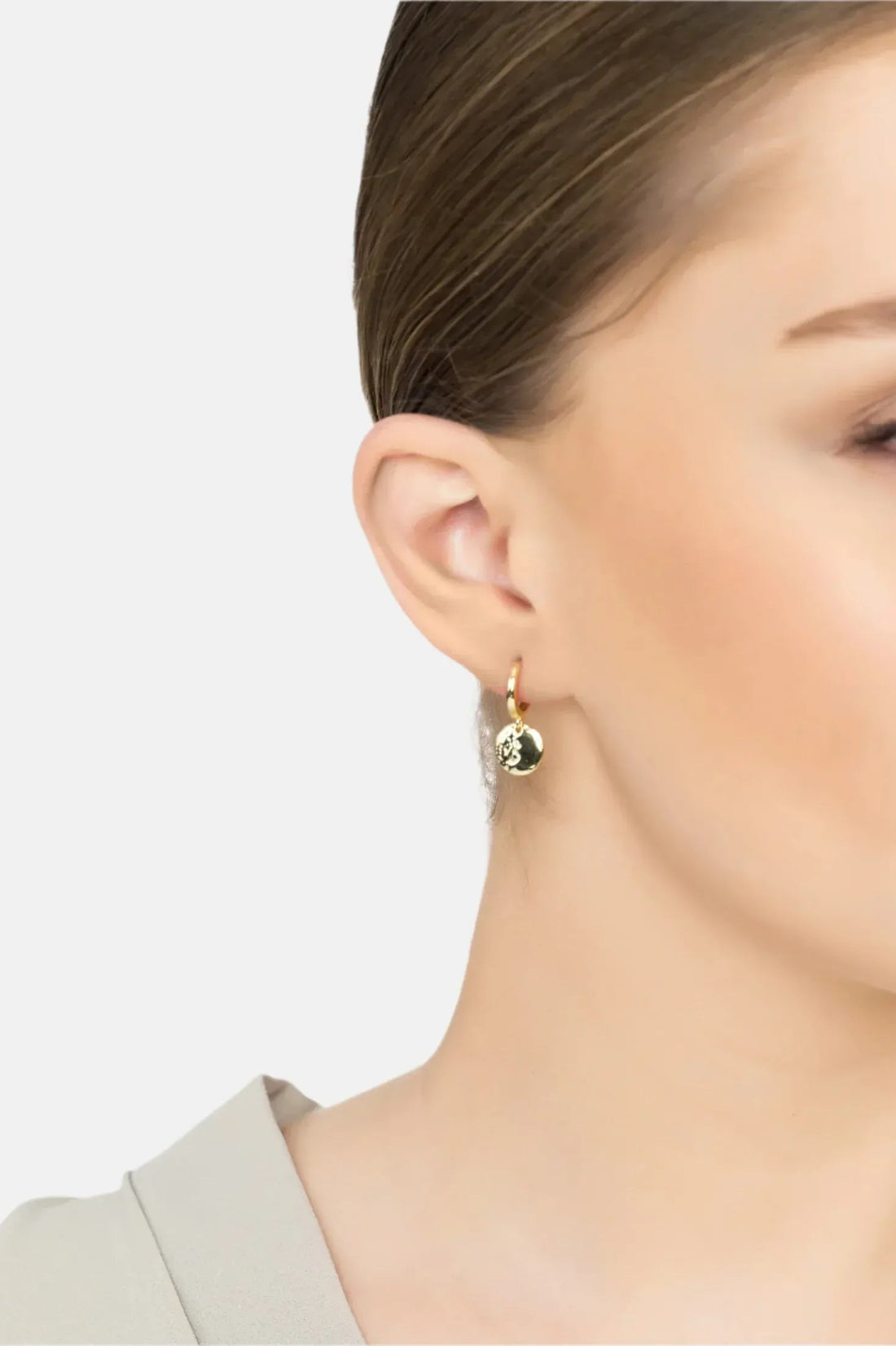 Gold huggie hoop earrings with round moon charm, worn on ear