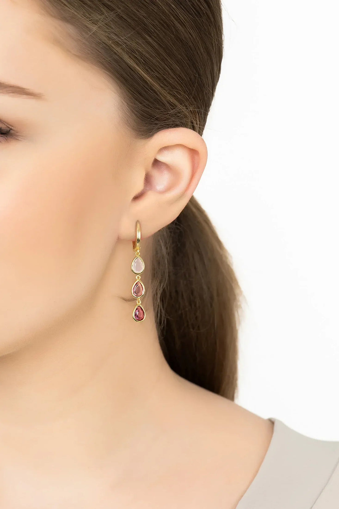 Gold triple teardrop drop earrings with pink stones on model ear