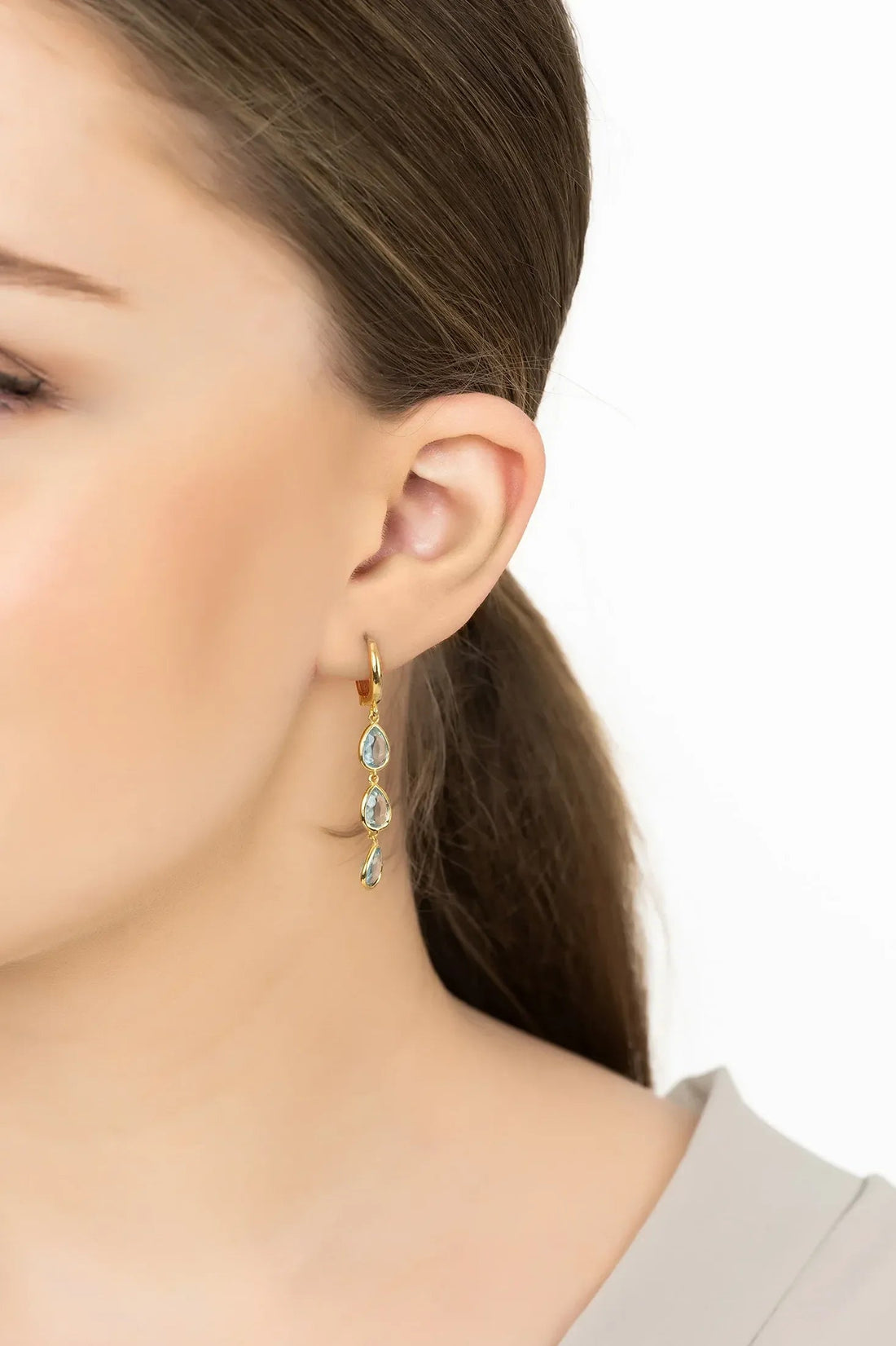 Gold triple teardrop blue topaz earrings on ear, side view