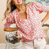 Orange floral V-neck puff-sleeve top with smocked bodice and short ruffled hem