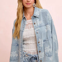 Light blue denim jacket with white floral print and button front, chest pocket detail
