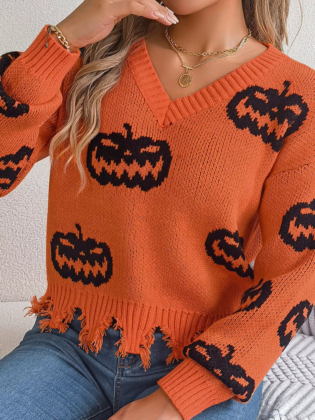 Orange knit V-neck sweater with black jack-o’-lantern pattern and fringe distressed bottom