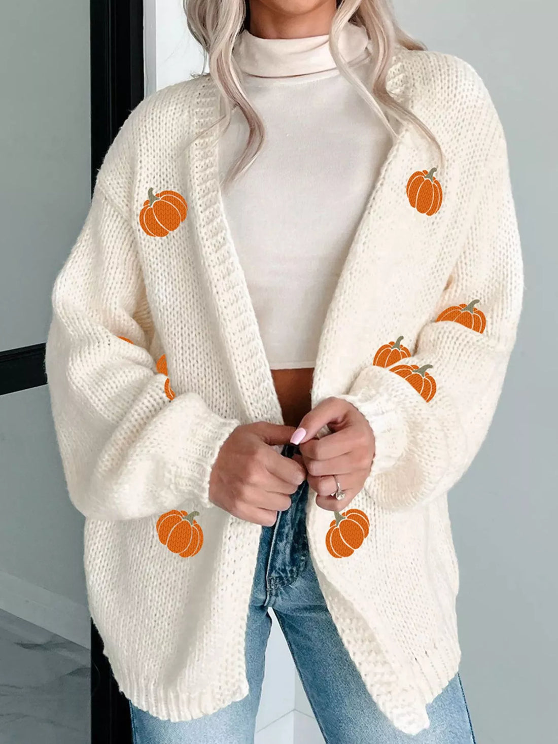 Cream knit cardigan with orange pumpkin embroidery accents and ribbed cuffs.