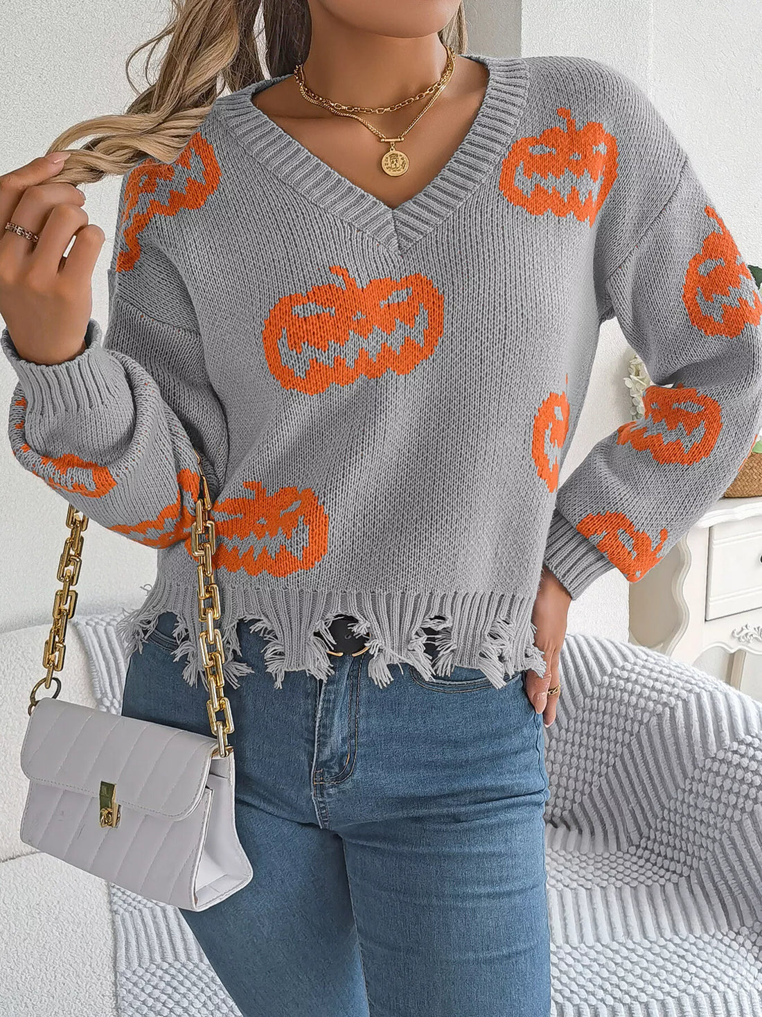 Gray pumpkin knit sweater with orange jack-o’-lantern motifs and ragged distressed hem