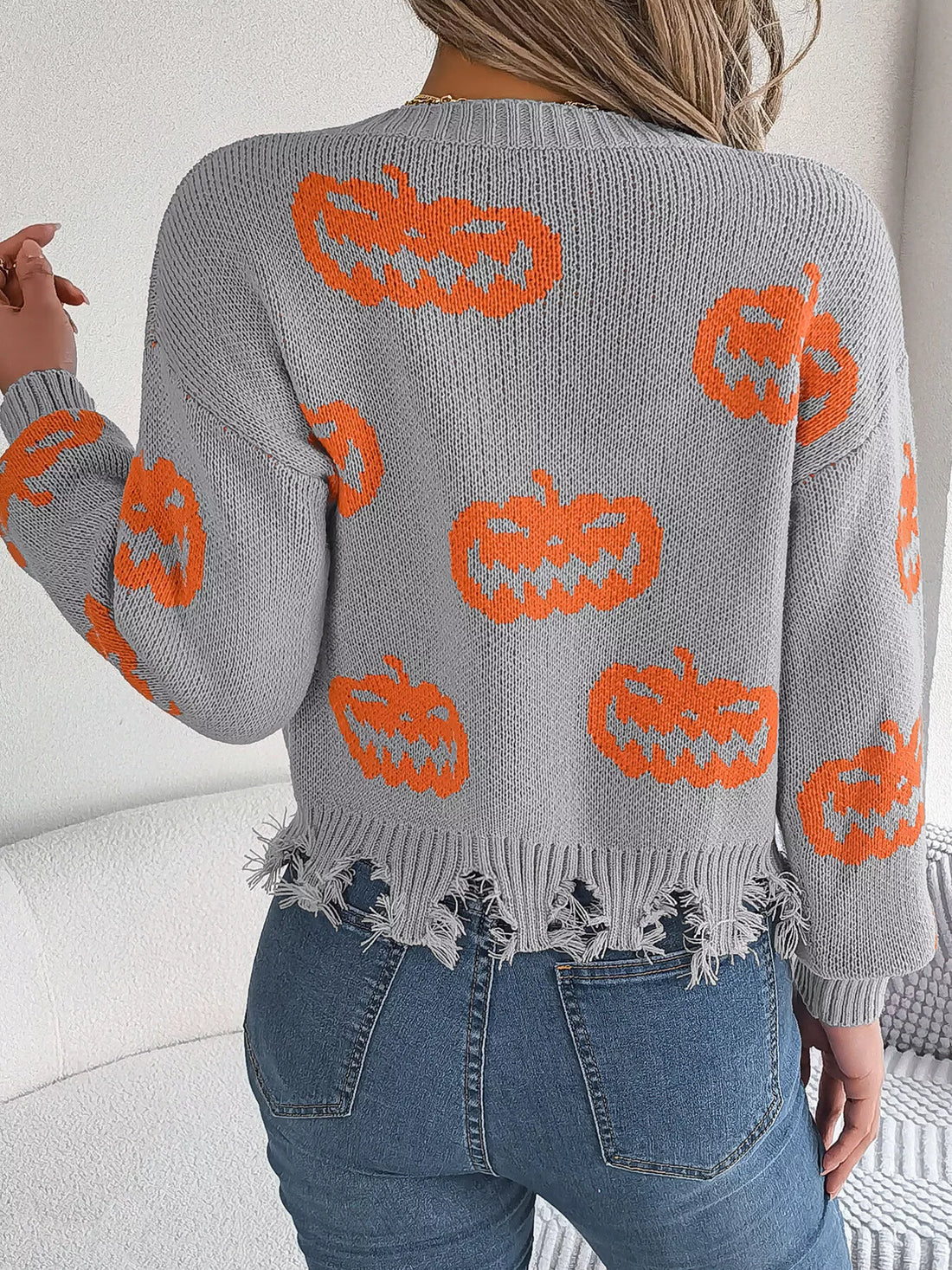 Back view of gray knit V-neck sweater with orange pumpkin pattern and distressed fringe hem