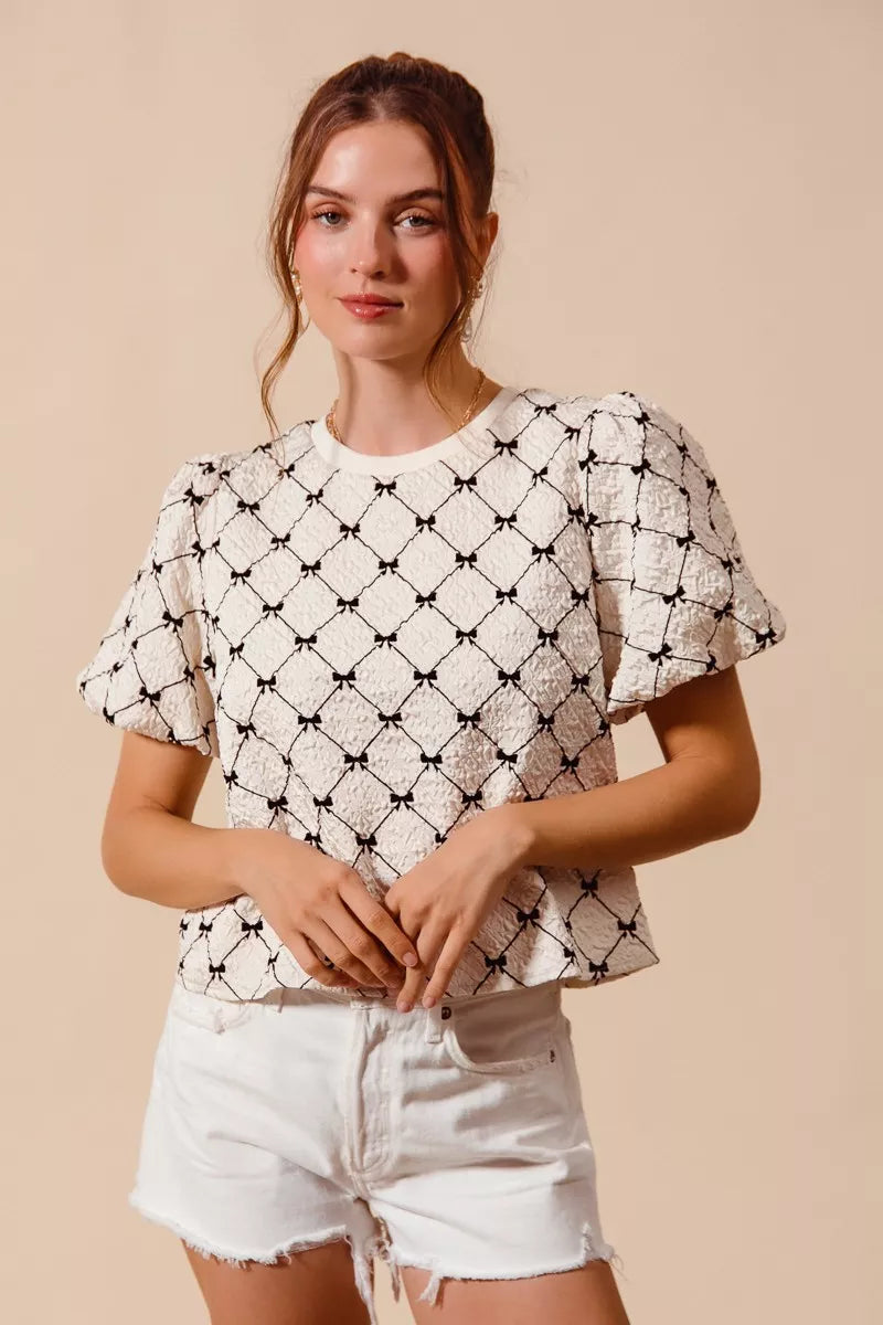 Ivory woven bubble sleeve top with black bow texture pattern and crew neckline