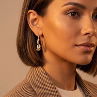 Gold snake hoop earrings with dangling sparkle details, worn by a model