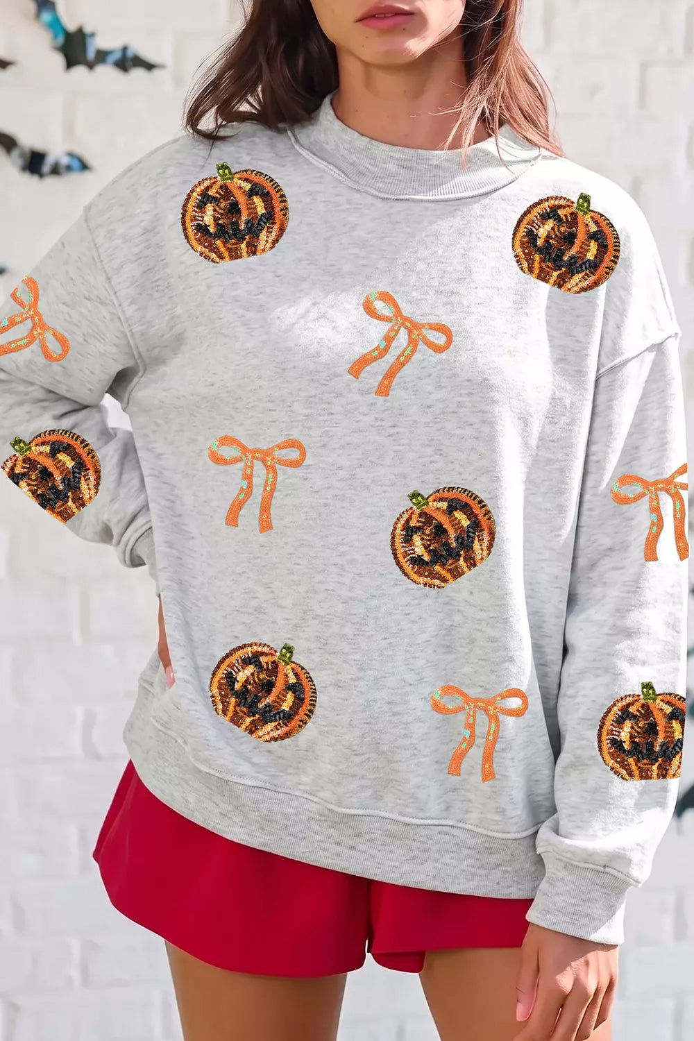 Light gray sweatshirt with orange sequin pumpkin faces and orange ribbon bow motifs