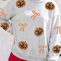Light gray sweatshirt with orange sequin pumpkin faces and orange ribbon bow motifs
