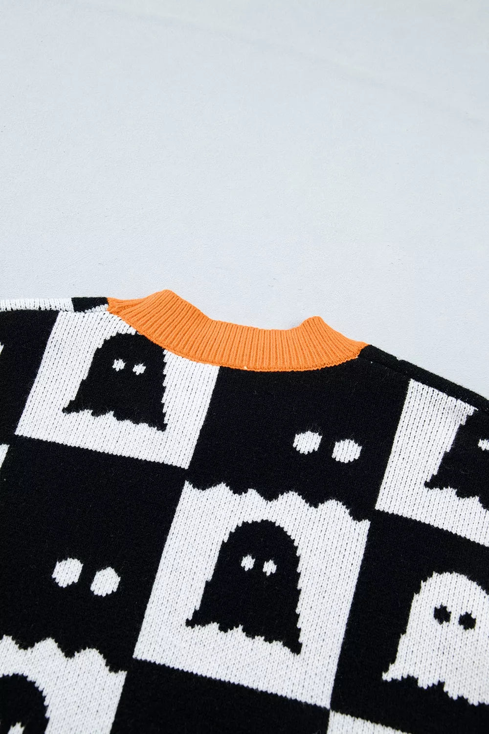 Black checkerboard ghost pattern sweater with orange ribbed collar