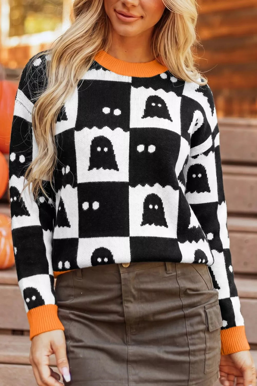 Black and white ghost checkerboard sweater featuring orange ribbed neckline and cuffs