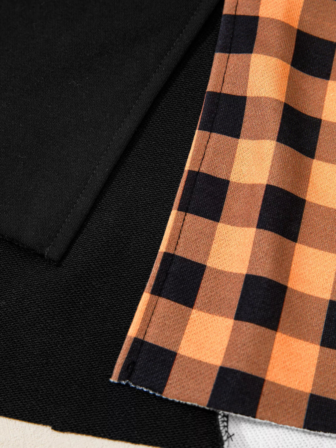 Close-up of black sleeve hem with orange and black plaid patch panel