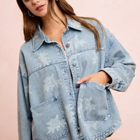 Light blue denim jacket with white floral print, button front, and chest flap pockets