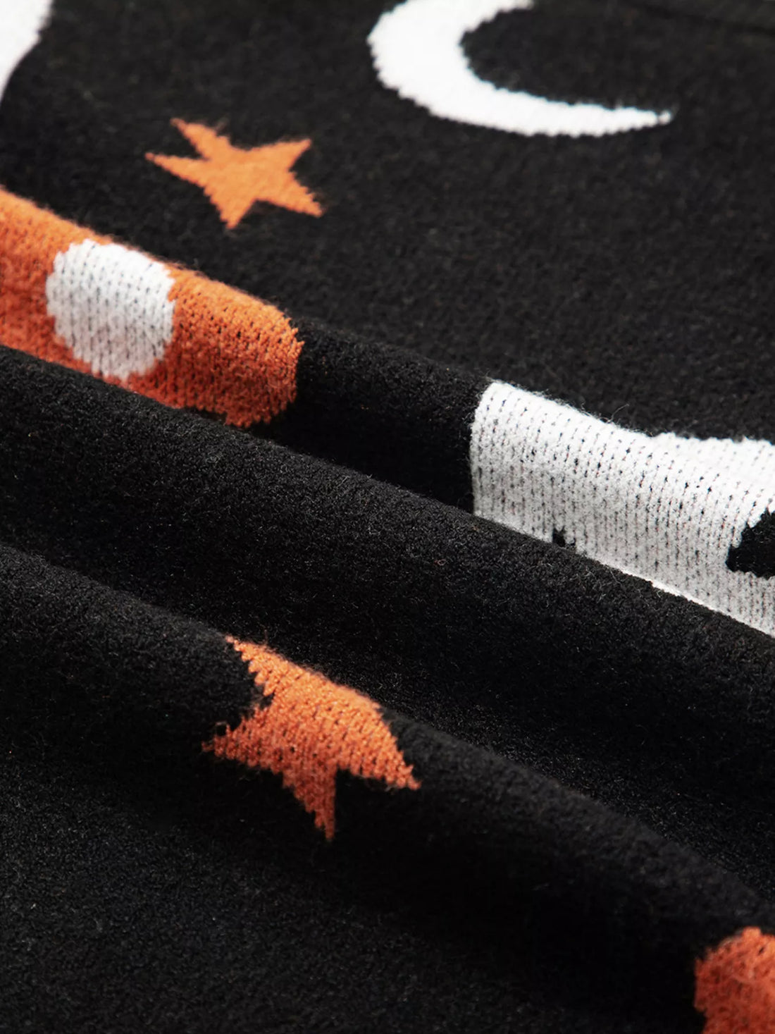 Black knit sleeve close-up with moon, star, and pumpkin-themed pattern detail