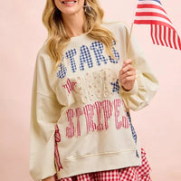 Cream sweatshirt with star-and-stripe patch lettering and red-blue bow graphic on side.