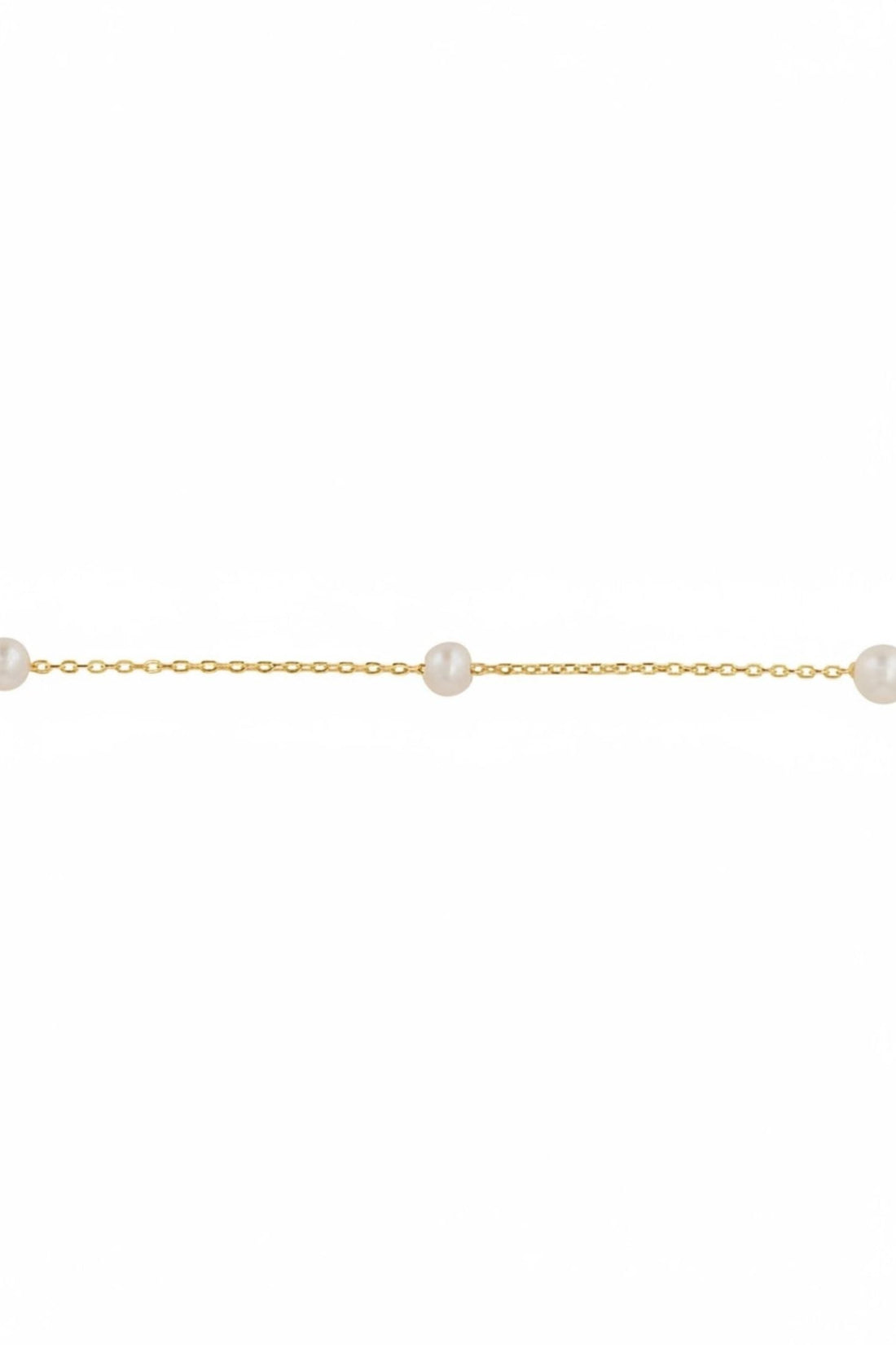 Close-up of gold chain bracelet with spaced round white pearls along the strand