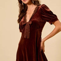 Burgundy velvet mini dress with lace-trim V-neck, tied bow, and gathered puff sleeves.
