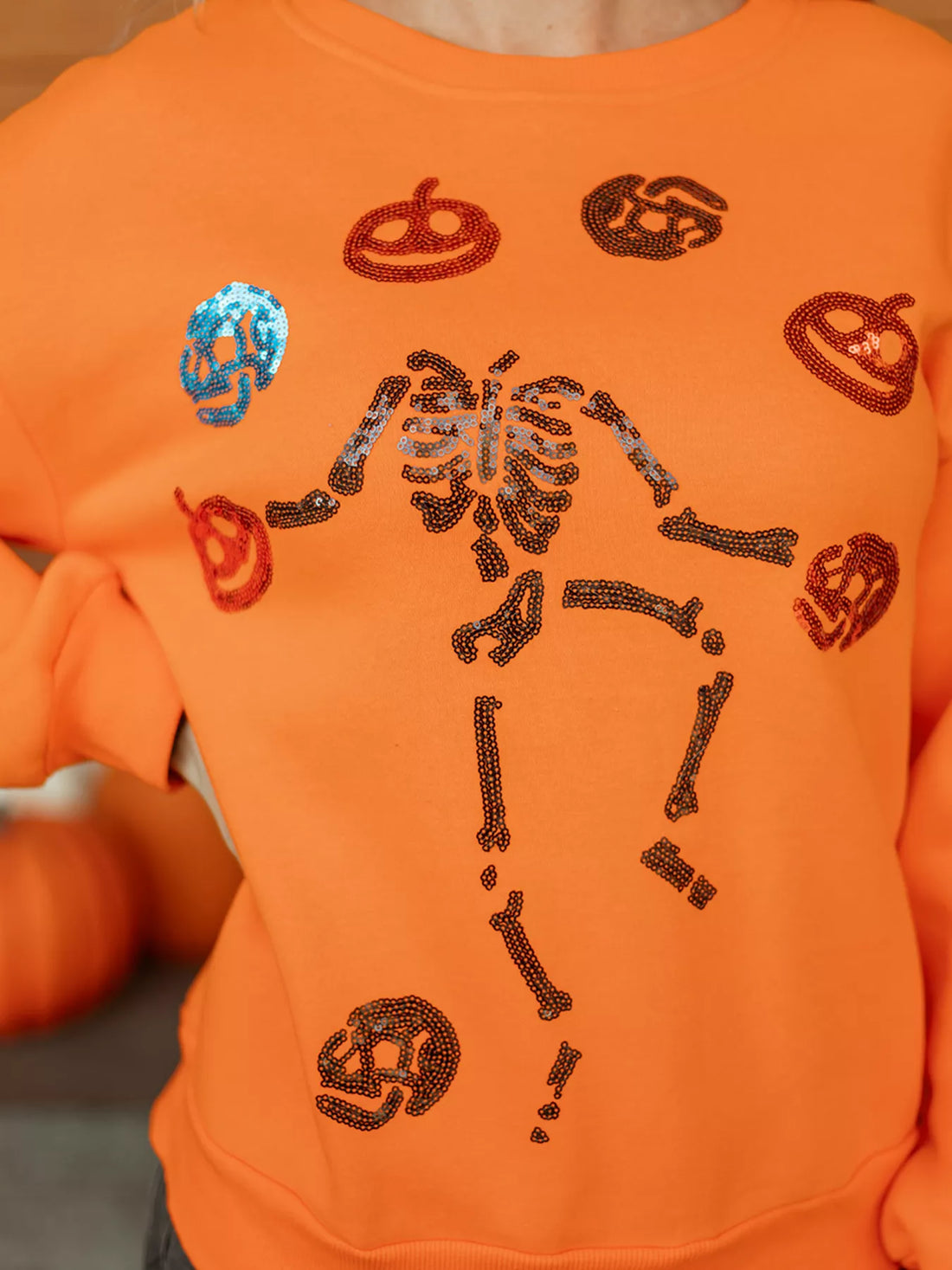 Orange sweatshirt close-up: sequin skeleton and icons across the front