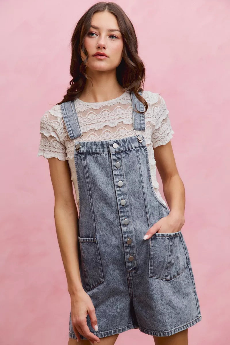 Light wash denim overall romper with adjustable straps, front buttons, and patch pockets