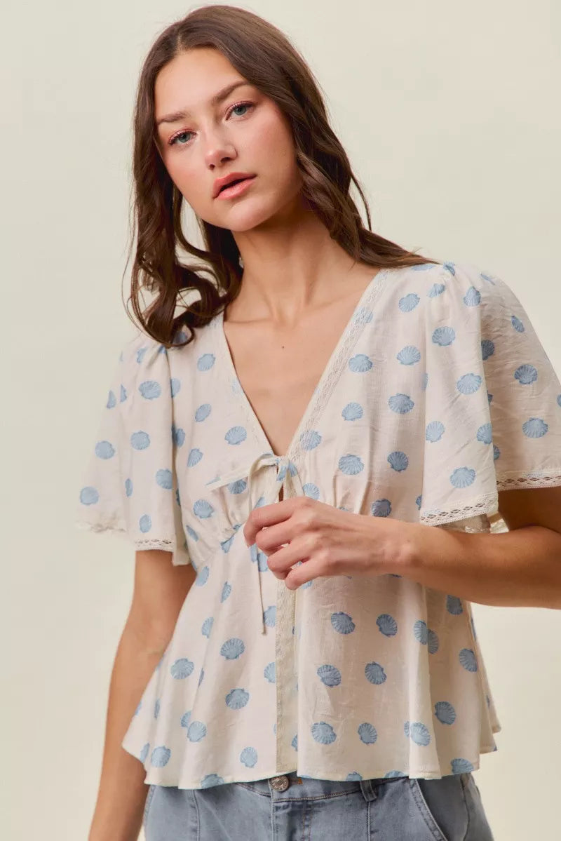 Ivory blouse with blue dot pattern, tie-front V-neck, and short flutter sleeves.