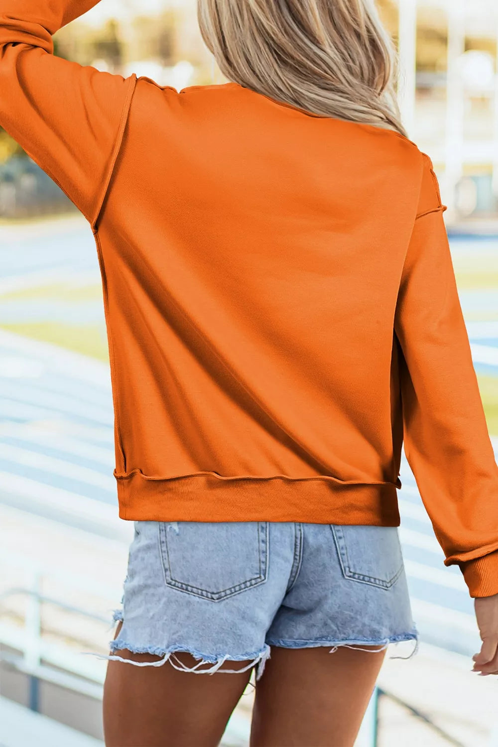 Orange mock neck sweatshirt, long sleeves, back view with curved hem