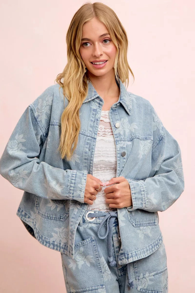 Light blue washed denim jacket with white floral print, button front, and flap pockets