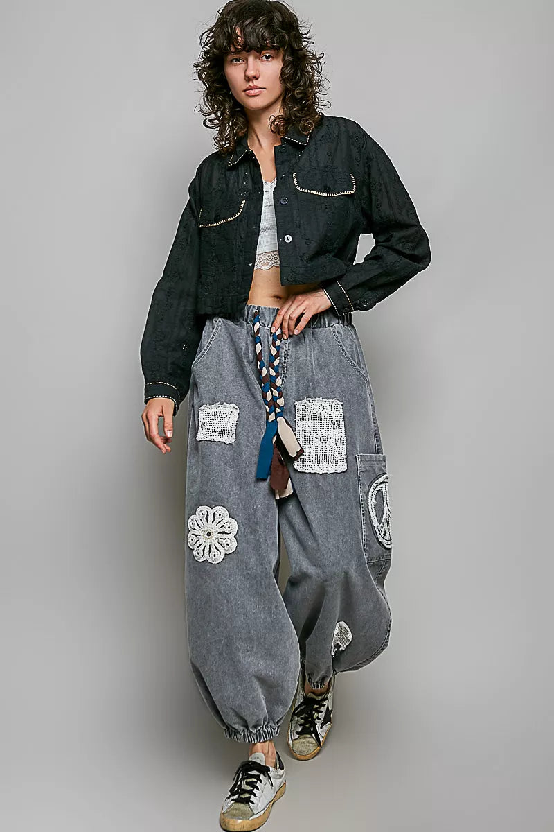 Black cropped eyelet cotton jacket with pointed collar and flap pockets, paired with gray harem pants.