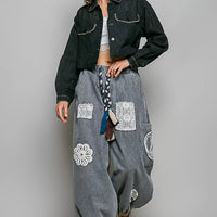 Black cropped eyelet cotton jacket with pointed collar and flap pockets, paired with gray harem pants.