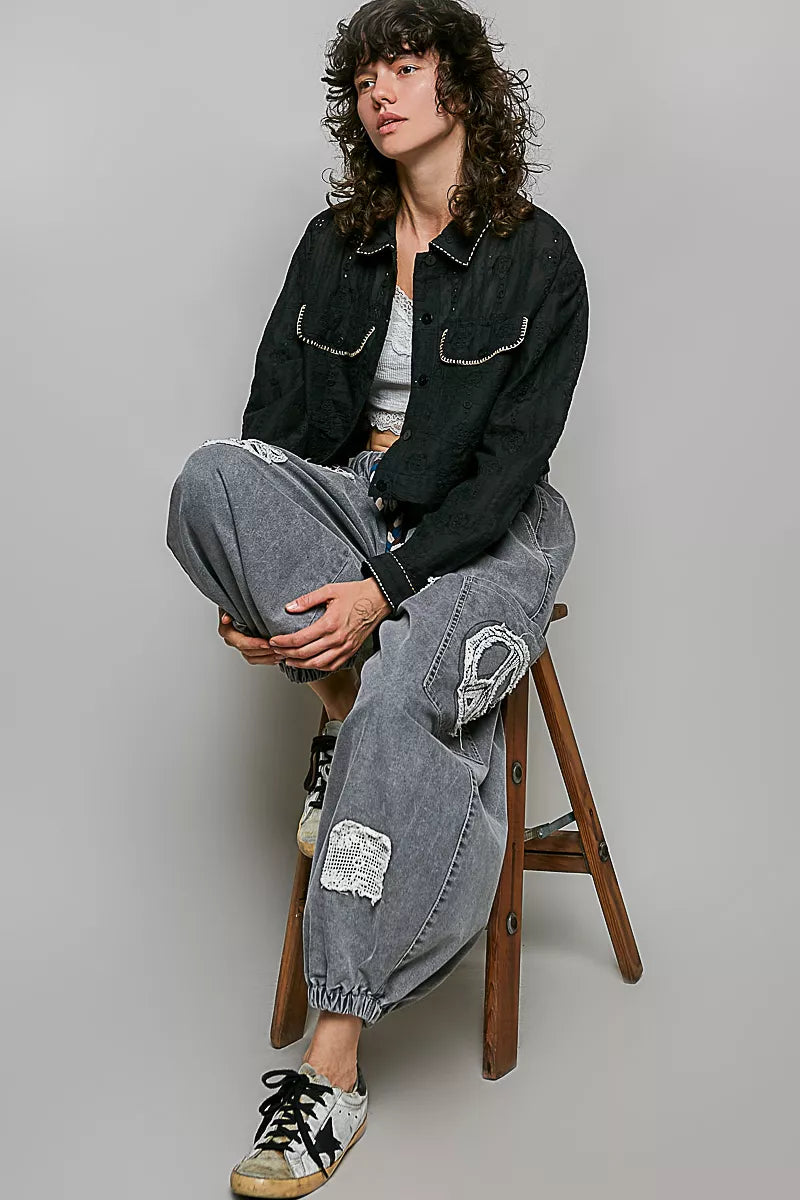 Black cropped button-front eyelet cotton jacket with contrast topstitching, worn with gray pants.