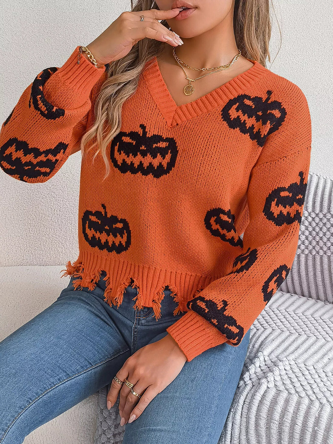 Orange V-neck sweater with black pumpkin motifs, frayed distressed hem and ribbed cuffs