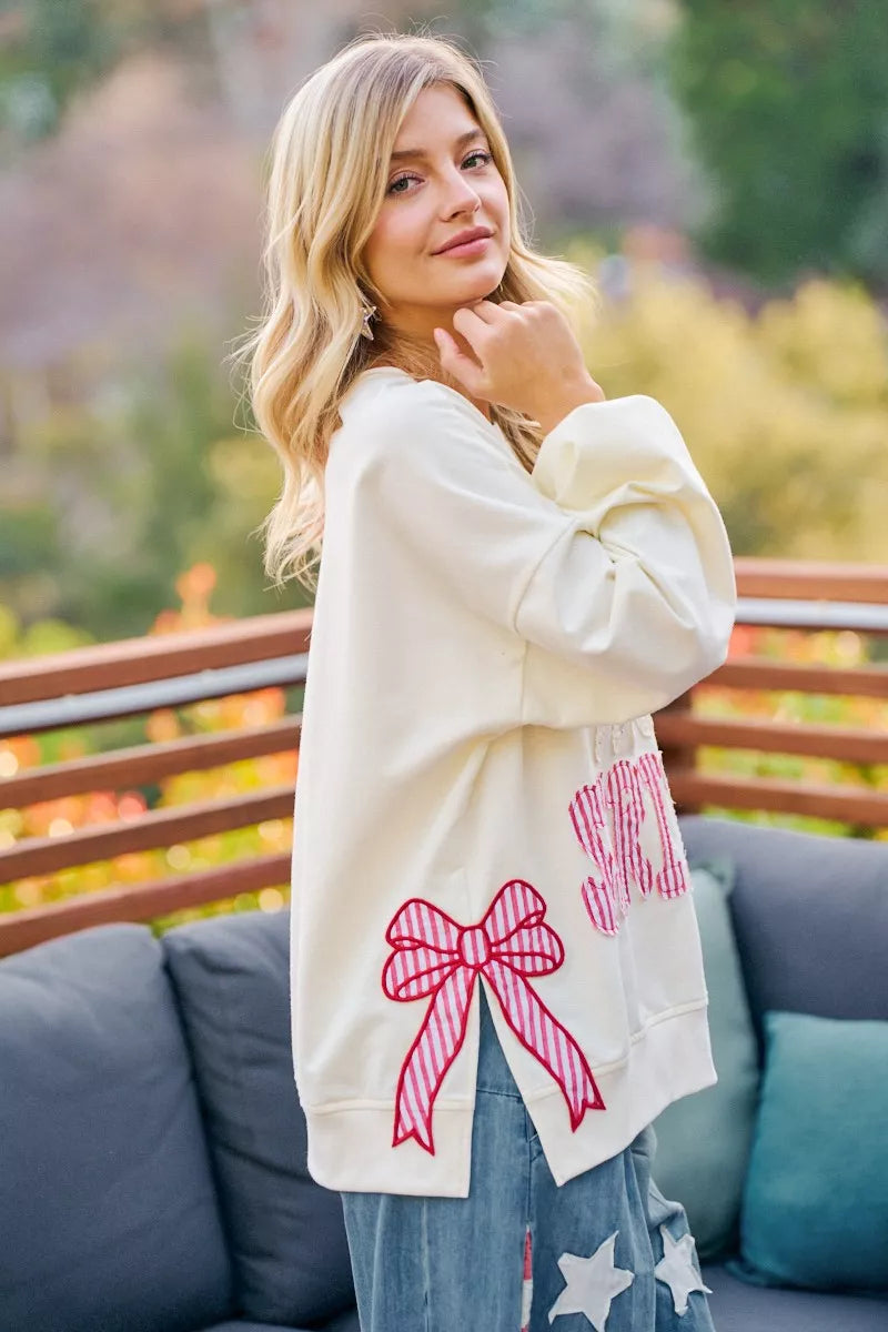 Cream sweatshirt with red bow patch, star detail, and striped graphic