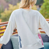 Cream sweatshirt back showing red and blue bow patches and side seam stitching.