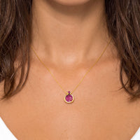 Gold pendant necklace with ruby-pink crystal-set pomegranate charm centered at neckline
