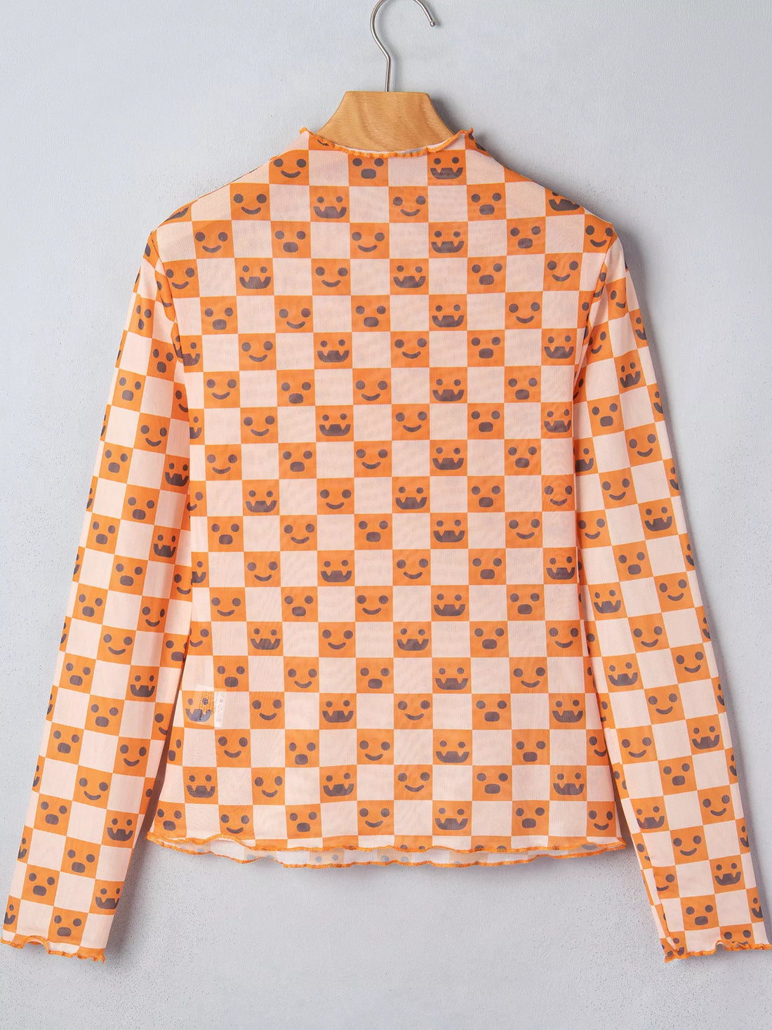 Back view of orange-and-white Halloween blouse on hanger with mock neck and jack-o’-lantern checker print