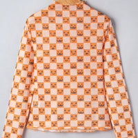 Back view of orange-and-white Halloween blouse on hanger with mock neck and jack-o’-lantern checker print