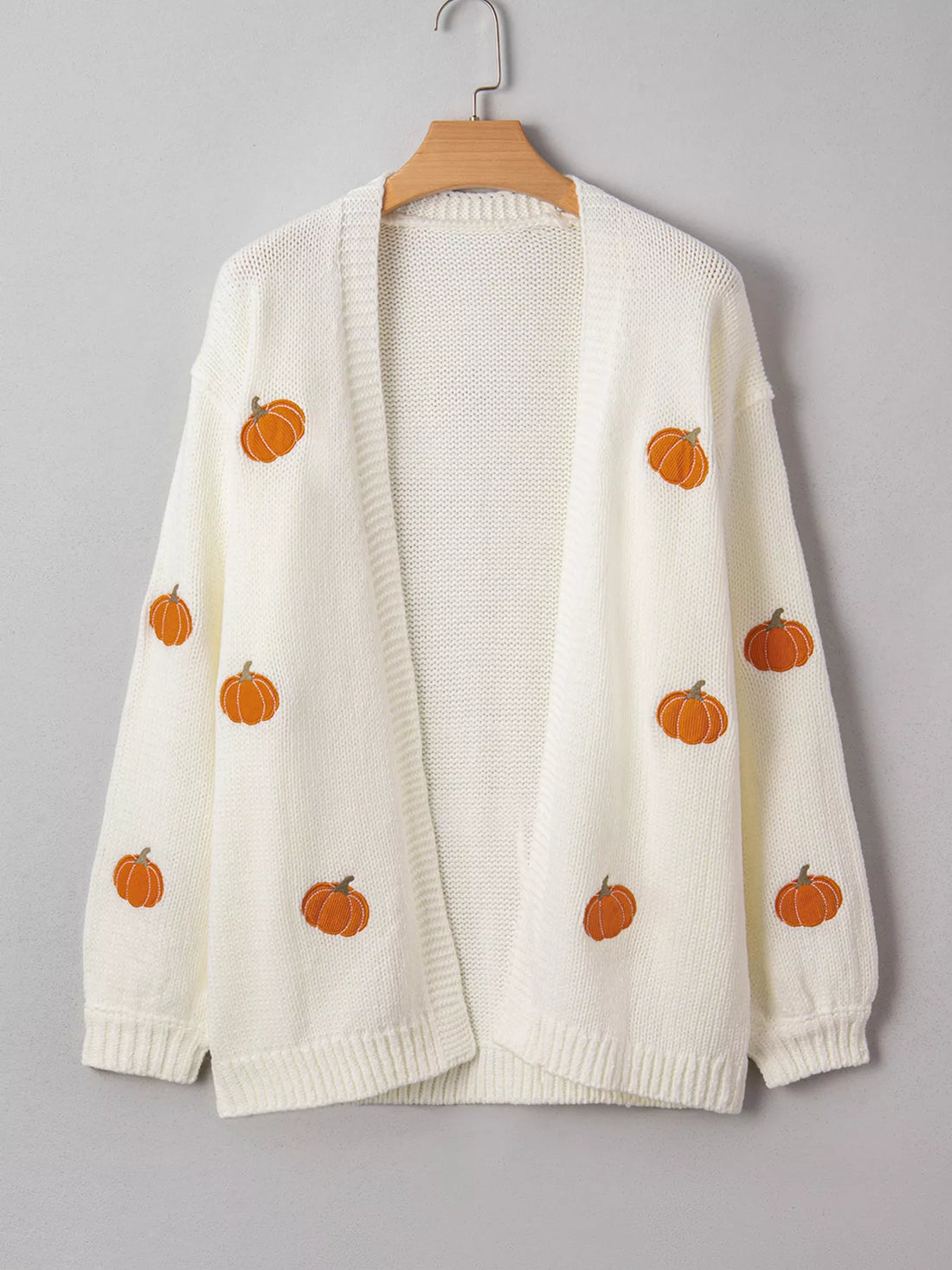 Off-white cardigan sweater on a hanger with scattered orange pumpkin embroidery.