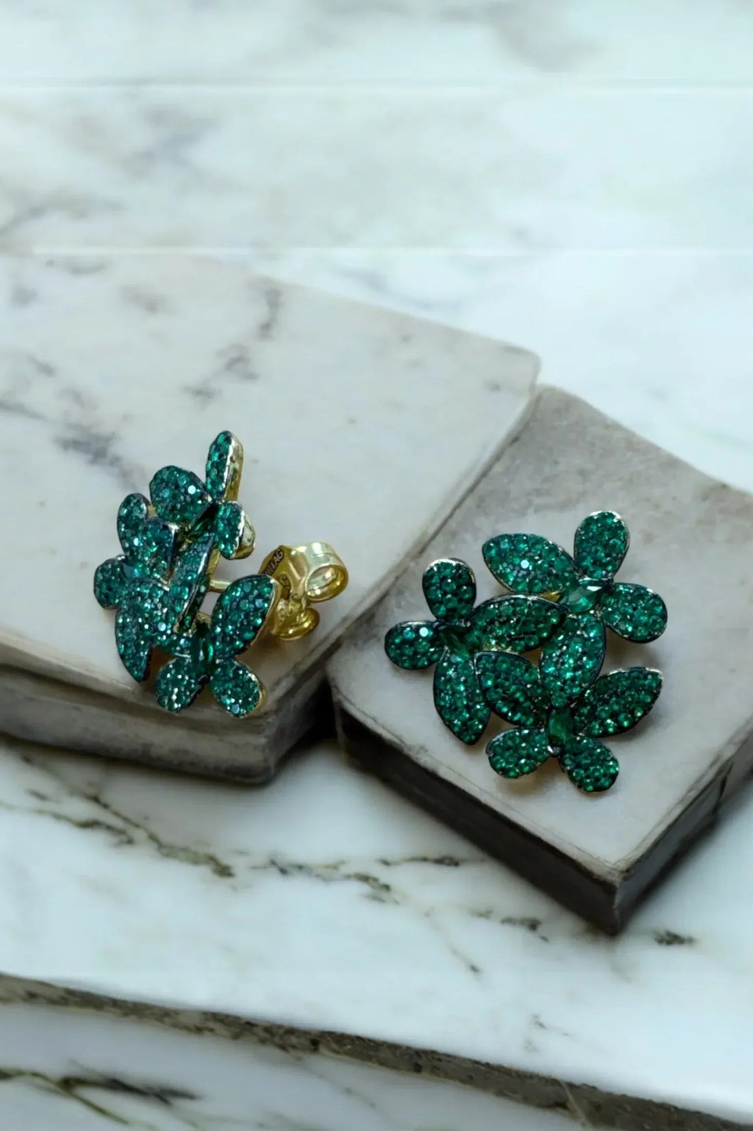 Close-up of emerald-green crystal flower stud earrings with gold-tone posts