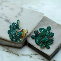 Close-up of emerald-green crystal flower stud earrings with gold-tone posts