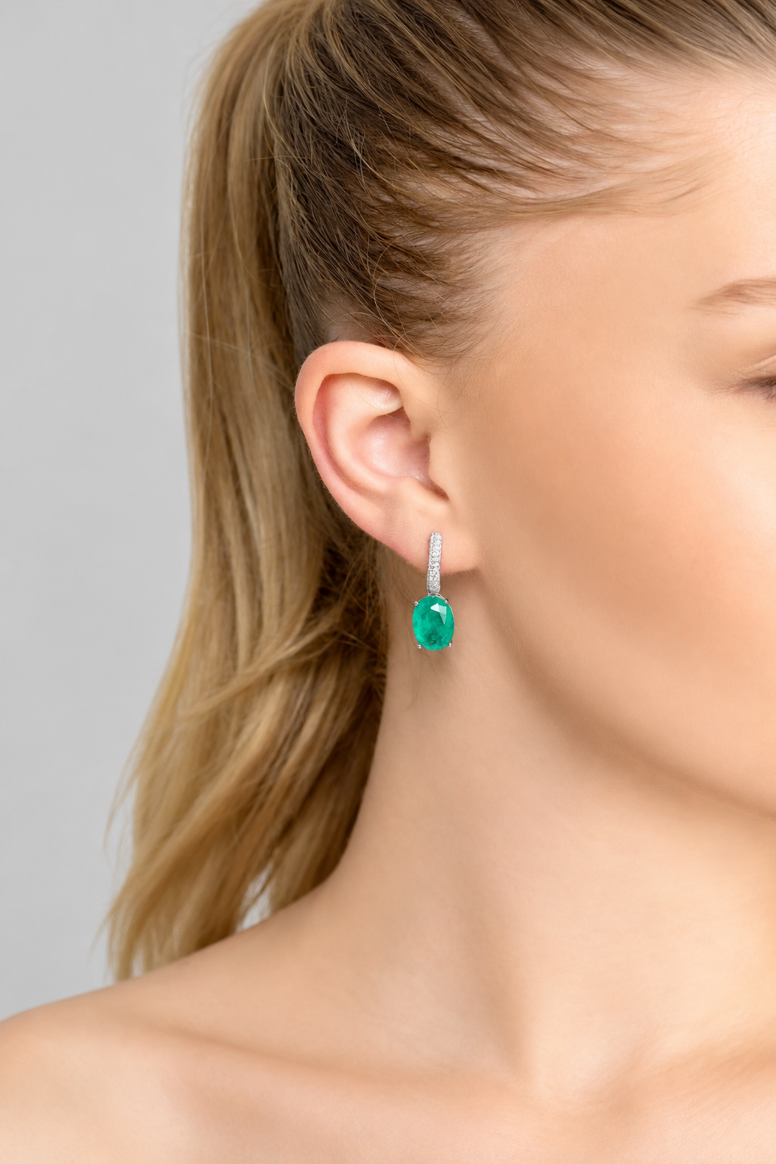 Silver drop earrings with emerald-green oval stone, worn on ear
