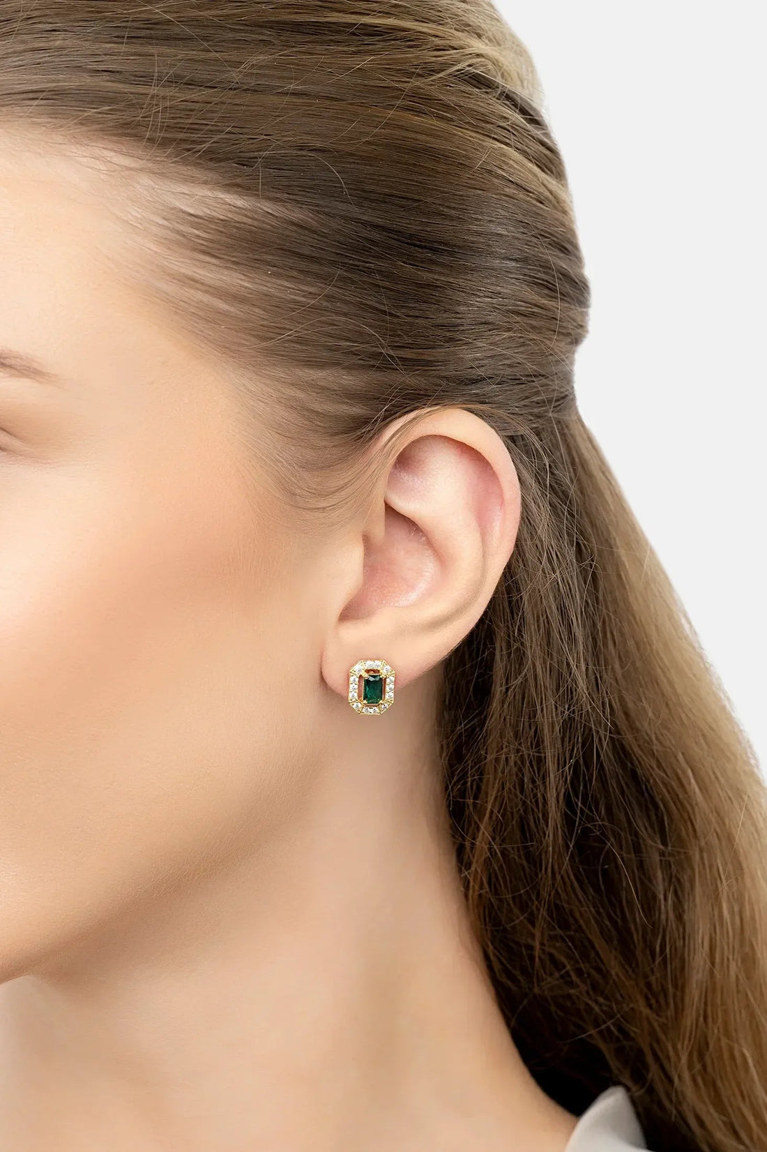 Gold emerald-green gemstone stud earrings with clear halo, side view