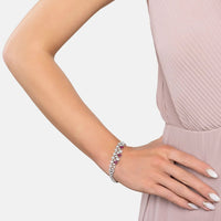 Silver tennis bracelet with clear stones and ruby teardrop charms worn on wrist.