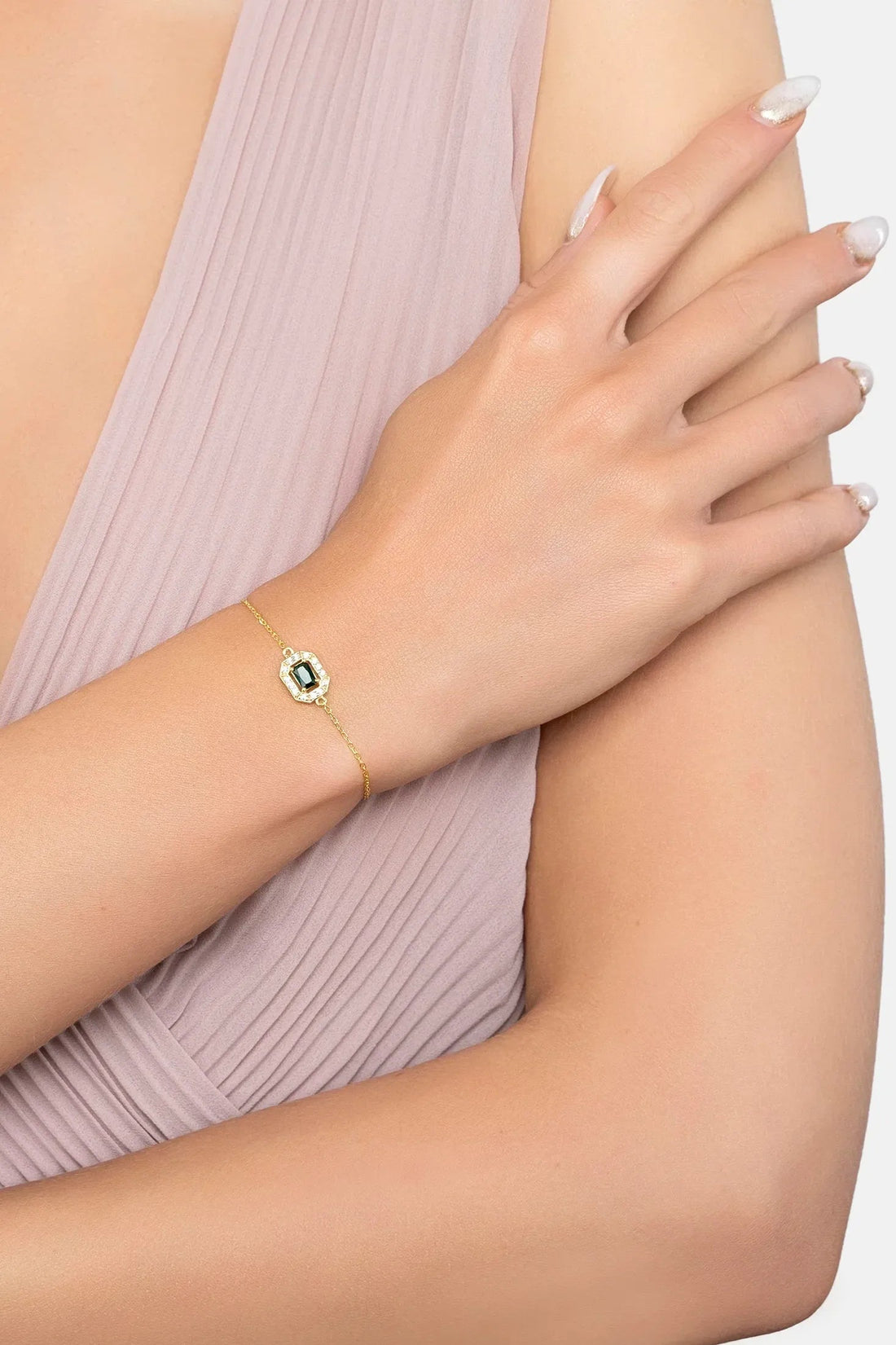 Emerald gemstone bracelet with gold chain worn on wrist