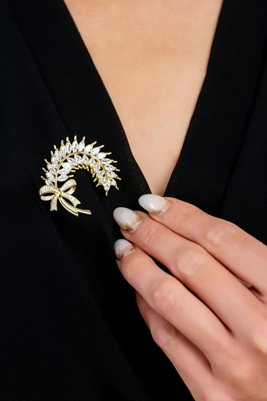 Gold ribbon and laurel leaf brooch with crystal-like stones on black clothing