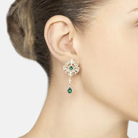 Gold drop earrings on model's ear with emerald-green teardrop drops and clear stones